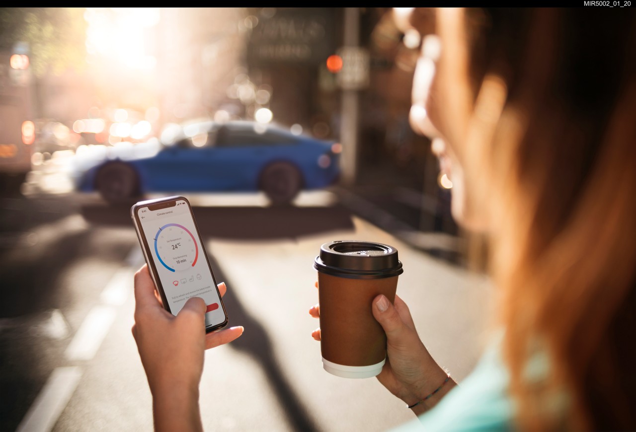 Close up a phone being held by the driver with the Toyota Mirai in the background.